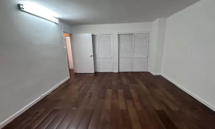 Unfurnished bedroom with dark wood-type flooring, baseboards, and two closets