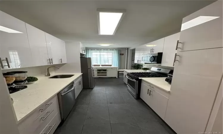 Kitchen with light stone counters, stainless steel appliances, dark tile patterned flooring, a sink, and white cabinetry