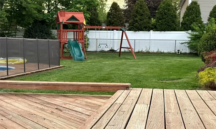 View of jungle gym with fence, a deck, and a yard