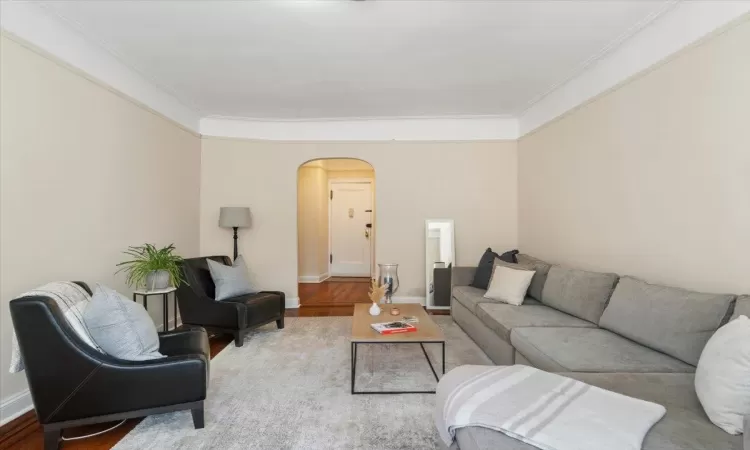 Living room with baseboards, crown molding, arched walkways, and wood finished floors