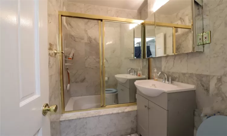 Full bathroom with tiled shower / bath, tile walls, vanity, and toilet