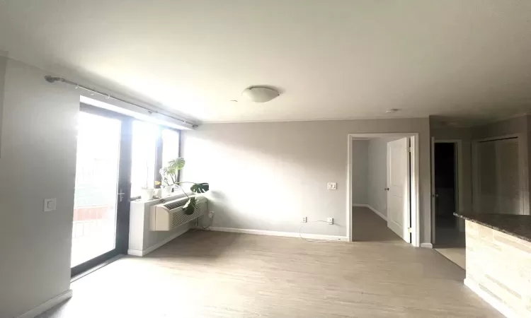 Unfurnished room featuring an AC wall unit, light wood-style flooring, and baseboards