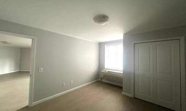 Unfurnished bedroom with a closet, a wall mounted air conditioner, wood finished floors, and baseboards