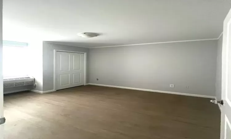 Unfurnished bedroom with baseboards, an AC wall unit, ornamental molding, a closet, and dark wood finished floors