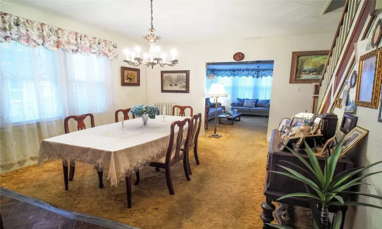 Carpeted dining space with plenty of natural light, stairway, and an inviting chandelier