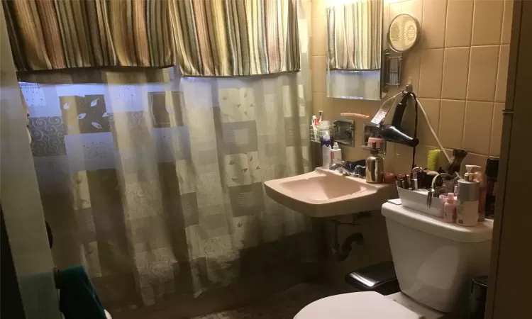 Bathroom featuring a shower with curtain, a sink, tile walls, and toilet