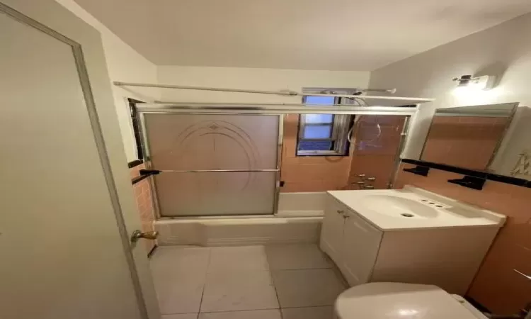 Bathroom featuring tile walls, toilet, combined bath / shower with glass door, vanity, and tile patterned floors