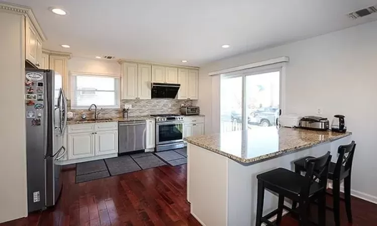 Kitchen featuring visible vents, appliances with stainless steel finishes, a peninsula, light stone countertops, and exhaust hood