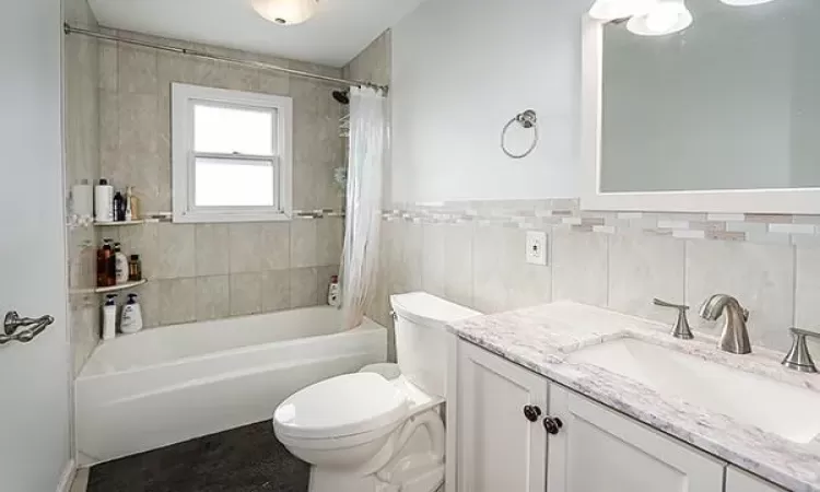 Bathroom with toilet, shower / tub combo, tile walls, and vanity