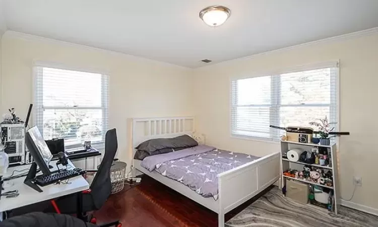 Bedroom with ornamental molding, multiple windows, wood finished floors, and visible vents