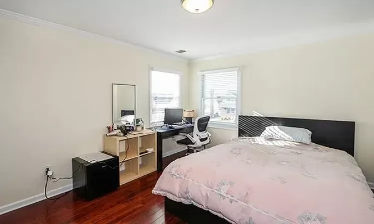 Bedroom with dark wood-style floors, ornamental molding, visible vents, and baseboards