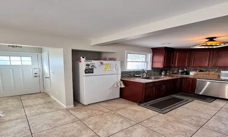 Kitchen featuring stainless steel dishwasher, a sink, freestanding refrigerator, and tasteful backsplash