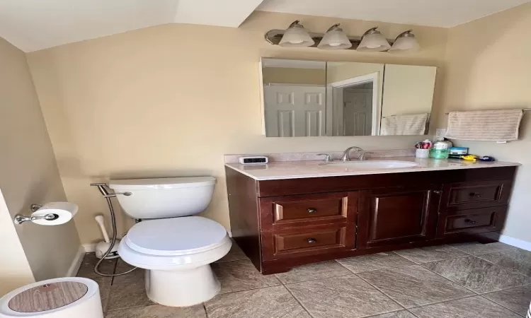 Bathroom with toilet, vaulted ceiling, vanity, and baseboards