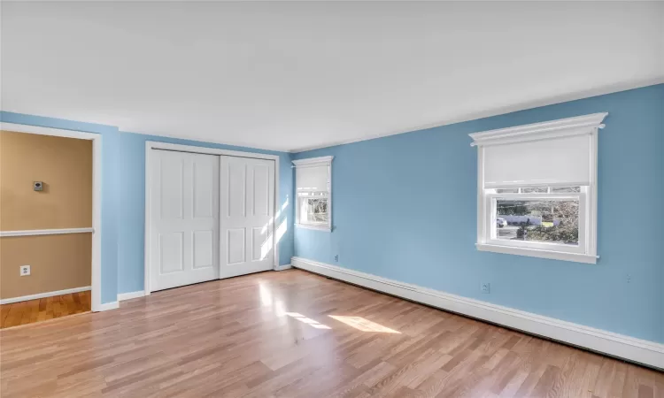 Unfurnished bedroom with light wood-type flooring, multiple windows, and a baseboard radiator