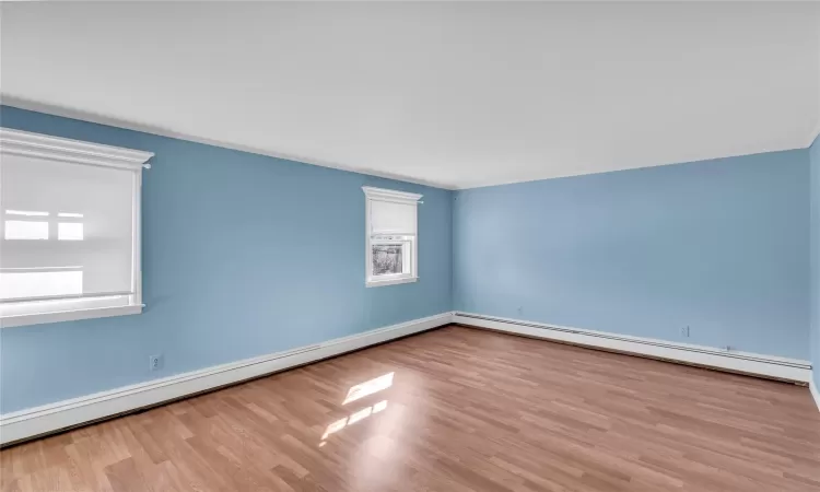 Unfurnished room featuring a baseboard heating unit, baseboards, and wood finished floors