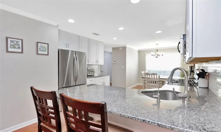 Kitchen featuring a peninsula, light stone countertops, a sink, and freestanding refrigerator