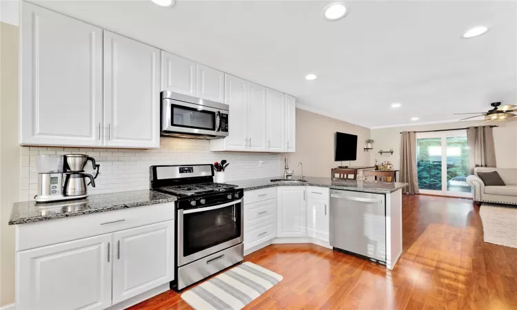 Kitchen featuring white cabinets, open floor plan, a peninsula, stainless steel appliances, and a sink