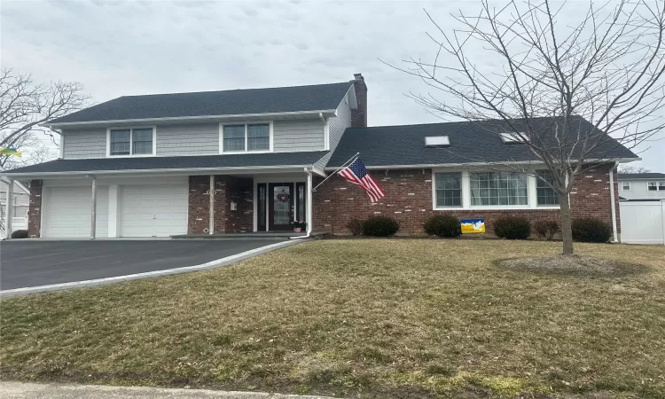 Traditional-style home with a front yard, a chimney, aphalt driveway, and brick siding