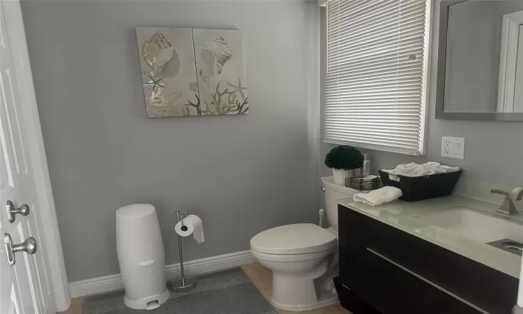 Half bath featuring toilet, tile patterned floors, baseboards, and vanity