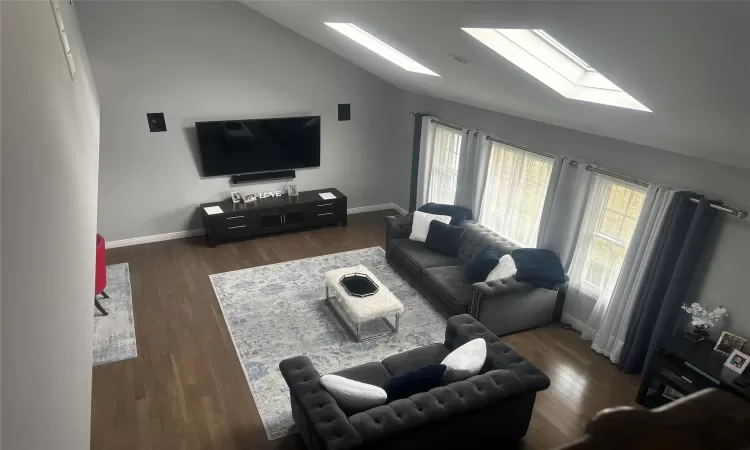 Living room featuring vaulted ceiling with skylight, baseboards, and wood finished floors