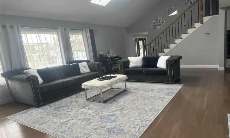 Living room with a skylight, dark wood-style flooring, stairway, high vaulted ceiling, and baseboards