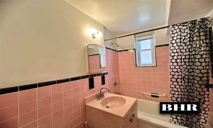 Bathroom with shower / bathing tub combination, wainscoting, vanity, and tile walls