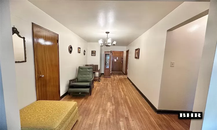 Hall with light wood-style flooring, baseboards, and a notable chandelier