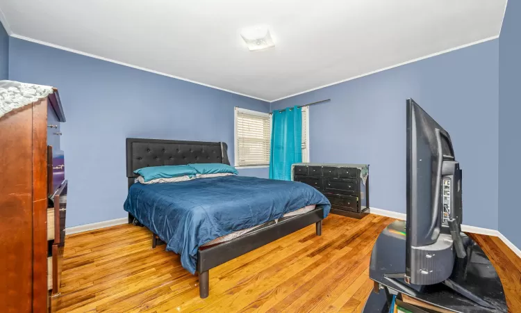 Bedroom with ornamental molding, wood finished floors, and baseboards