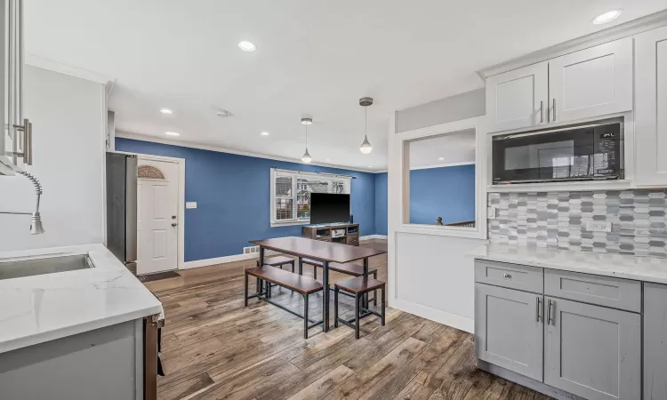 Kitchen featuring tasteful backsplash, dark wood-type flooring, gray cabinetry, black microwave, and a sink