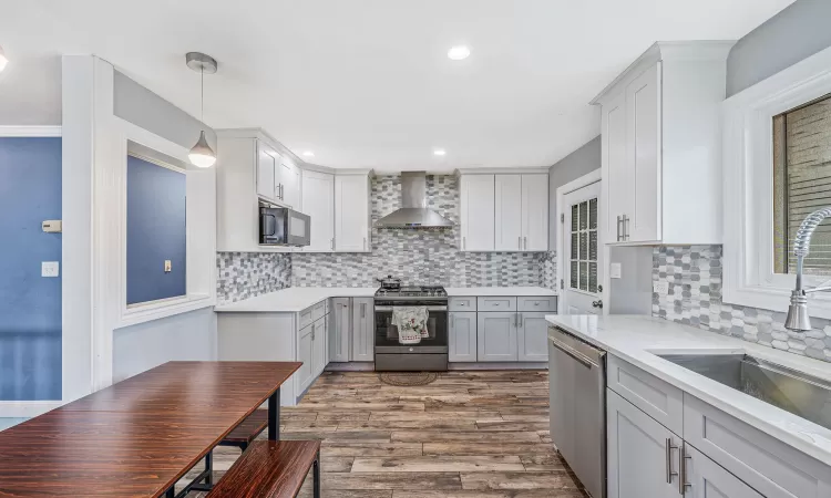 Kitchen with stainless steel appliances, a sink, wall chimney range hood, dark wood-style floors, and decorative light fixtures