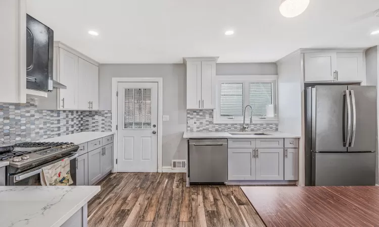 Kitchen featuring light stone counters, dark wood finished floors, stainless steel appliances, visible vents, and a sink