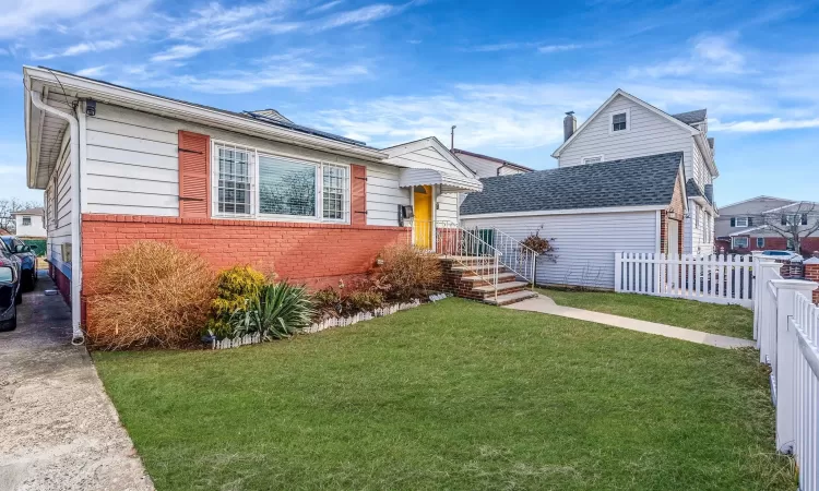 View of front of house with brick siding, a front yard, and fence