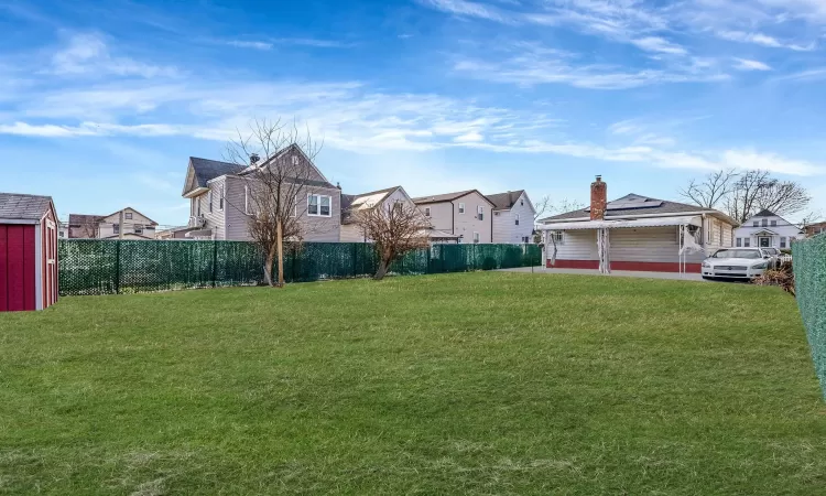 View of yard featuring a storage unit, an outdoor structure, a fenced backyard, and a residential view