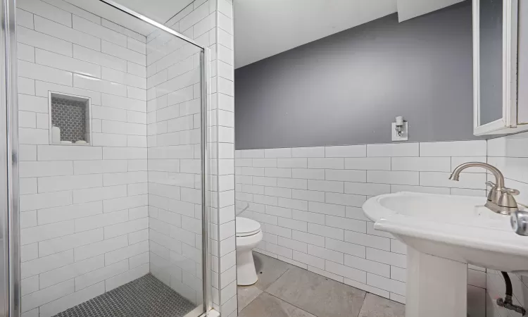 Full bathroom with toilet, tile walls, wainscoting, a shower stall, and tile patterned floors