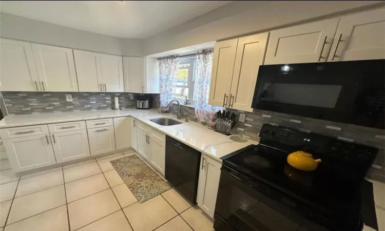 Kitchen with white cabinetry, a sink, black appliances, and light tile patterned floors