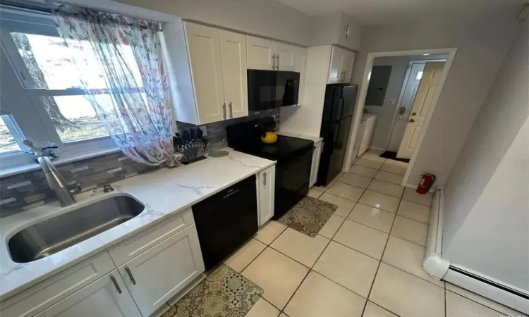 Kitchen featuring light tile patterned floors, tasteful backsplash, white cabinetry, a sink, and black appliances