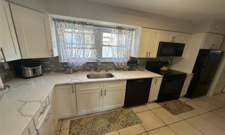 Kitchen featuring tasteful backsplash, white cabinets, a sink, and black appliances