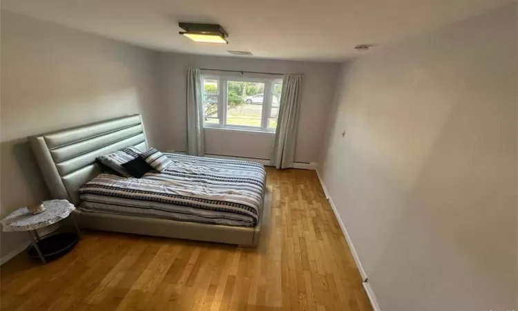 Bedroom featuring a baseboard radiator, visible vents, baseboards, and wood finished floors