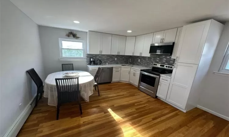 Kitchen with decorative backsplash, appliances with stainless steel finishes, light countertops, light wood-type flooring, and a sink