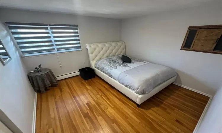 Bedroom featuring baseboard heating, light wood-type flooring, and baseboards