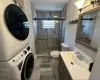 Bathroom featuring vanity, stacked washer / dryer, a shower stall, and toilet