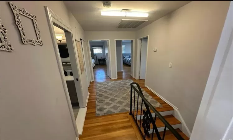 Hallway featuring baseboards, visible vents, an upstairs landing, and wood finished floors