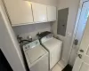 Washroom featuring cabinet space, light tile patterned floors, electric panel, baseboards, and washing machine and clothes dryer