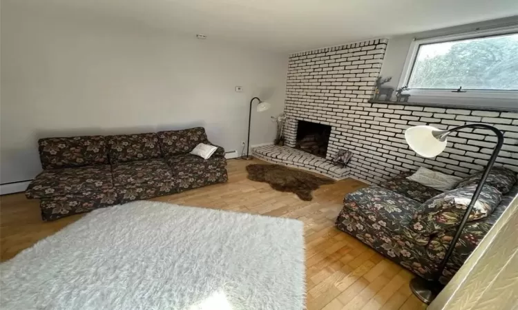 Living room with a baseboard radiator, a brick fireplace, brick wall, and wood finished floors