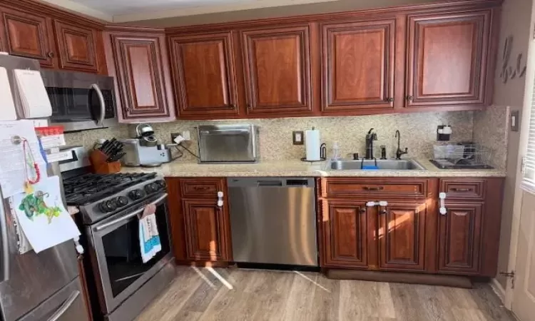 Kitchen featuring light stone counters, a sink, light wood-style floors, appliances with stainless steel finishes, and backsplash