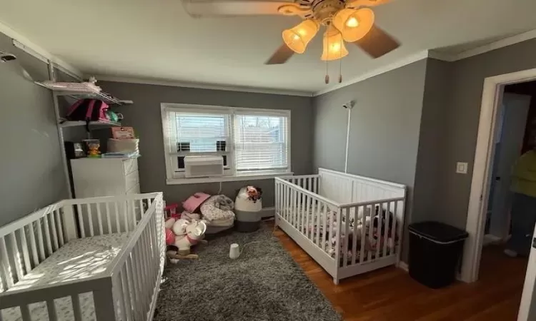 Bedroom with cooling unit, wood finished floors, a ceiling fan, a nursery area, and crown molding