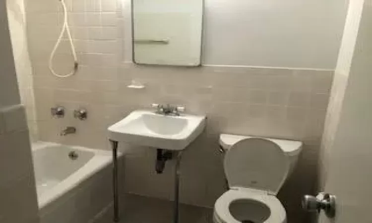 Bathroom featuring toilet, a sink,  shower combination, and tile walls