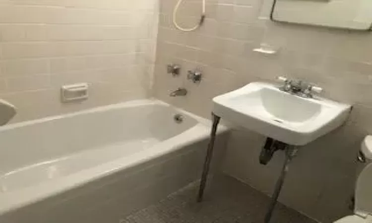 Full bathroom featuring toilet, a sink, tile walls, shower / washtub combination, and tile patterned floors