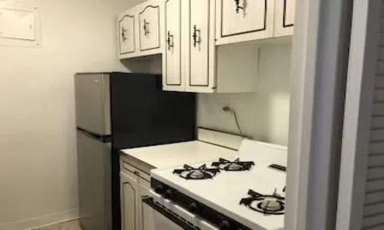 Kitchen featuring white range with gas stovetop, baseboards, light countertops, electric panel, and freestanding refrigerator