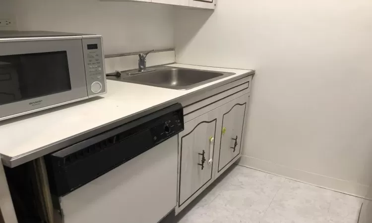 Kitchen with white dishwasher, a sink, baseboards, marble finish floor, and light countertops